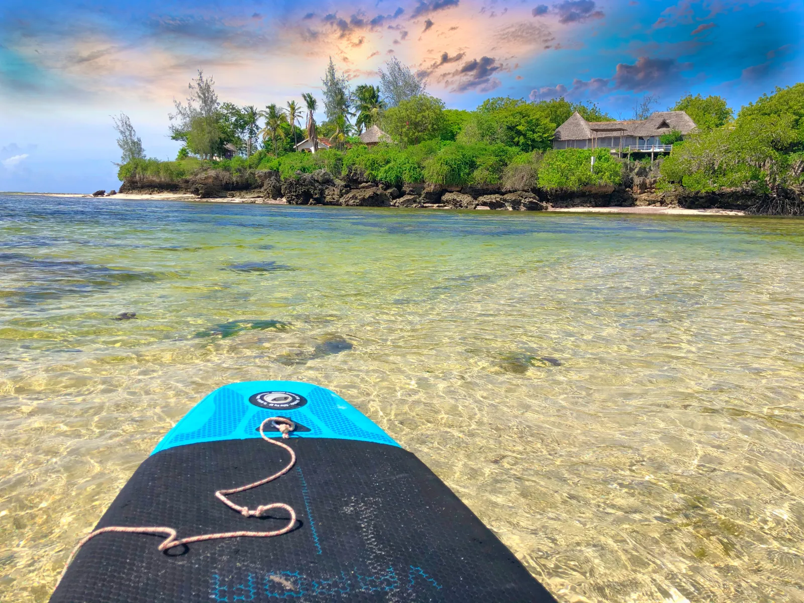 Paddleboarding over clear shallow water toward The Rock & Sea