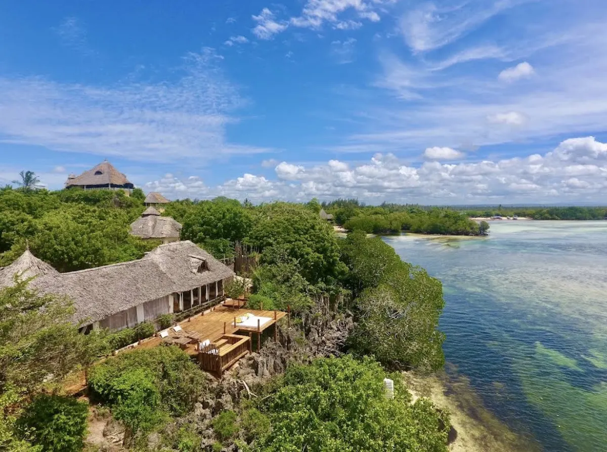 Aerial view of the thatched lodges of The Rock & Sea on their coral cliff above the turquoise channel of Mida Creek