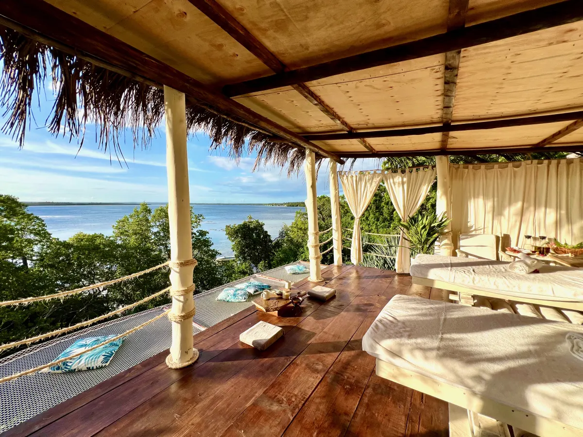 A shaded open-air massage deck with two treatment beds overlooking the creek