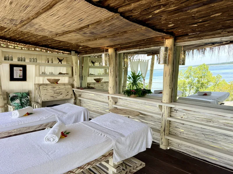 Two open-air treatment beds under the makuti roof at Jua Spa, facing the creek