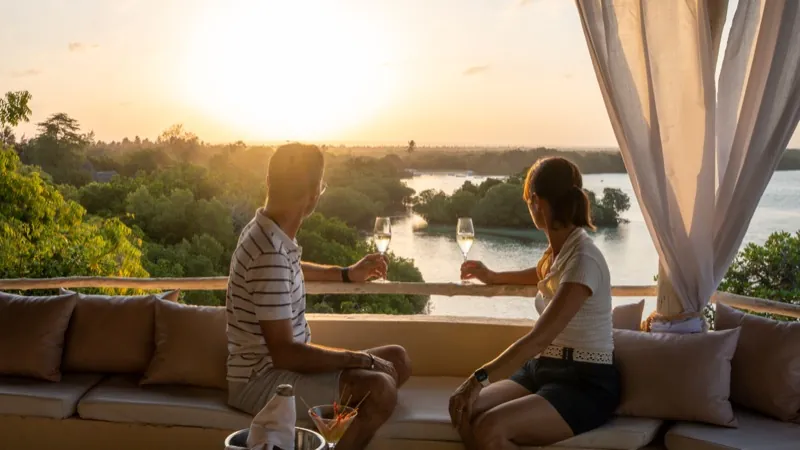 Two guests raising a glass on the cushioned sunset lounge as the sun goes down over Mida Creek