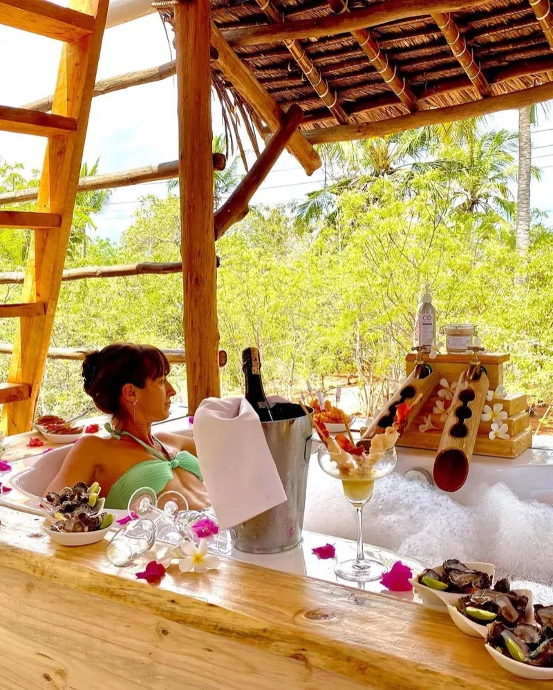 A table for two set with roses and petals on the white sand at the water's edge